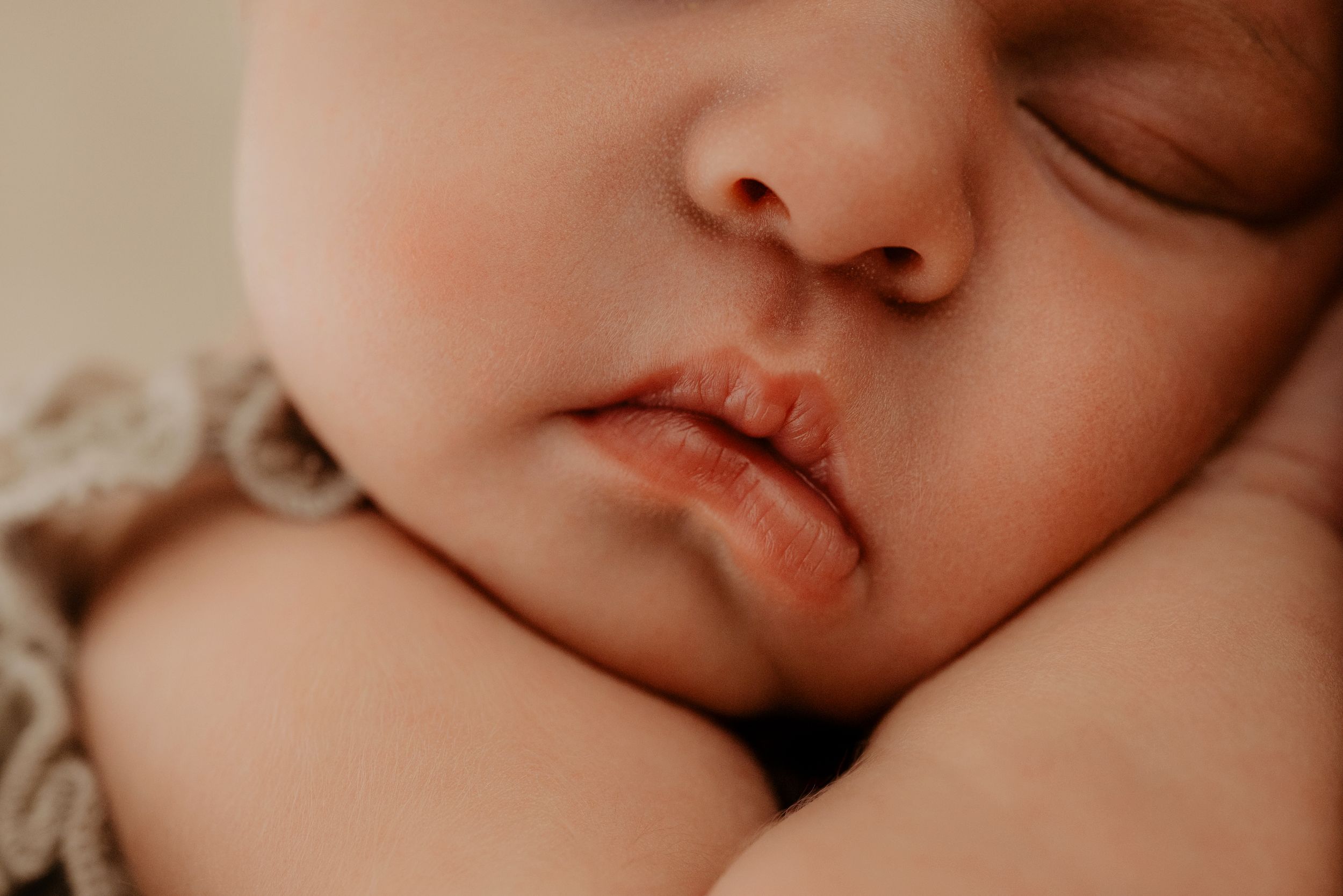 Sweet newborn sleeping peacefully in a soft neutral setting with a gentle, serene expression.