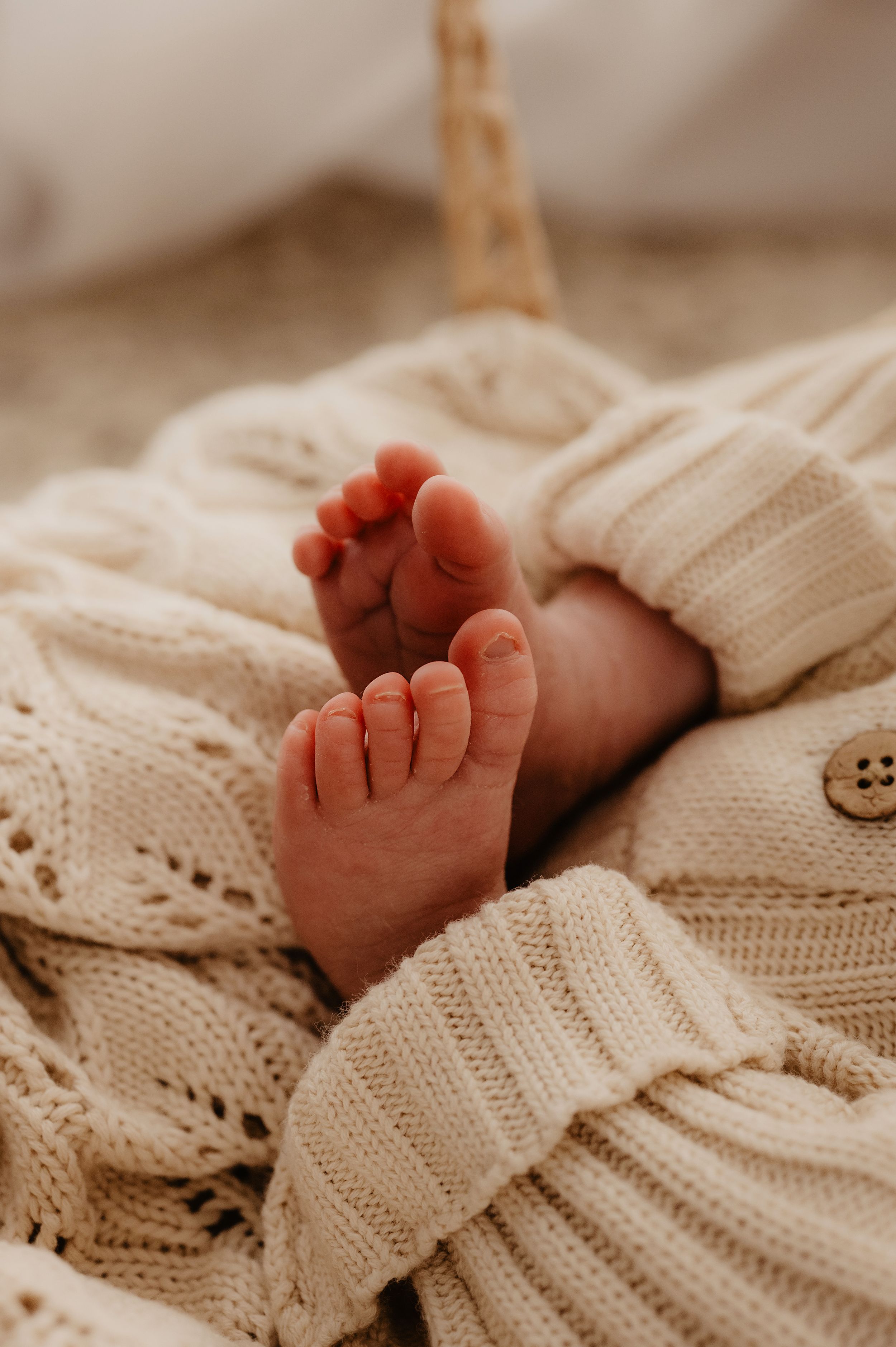 Tiny newborn feet peeking out from a cozy cream knitted blanket.