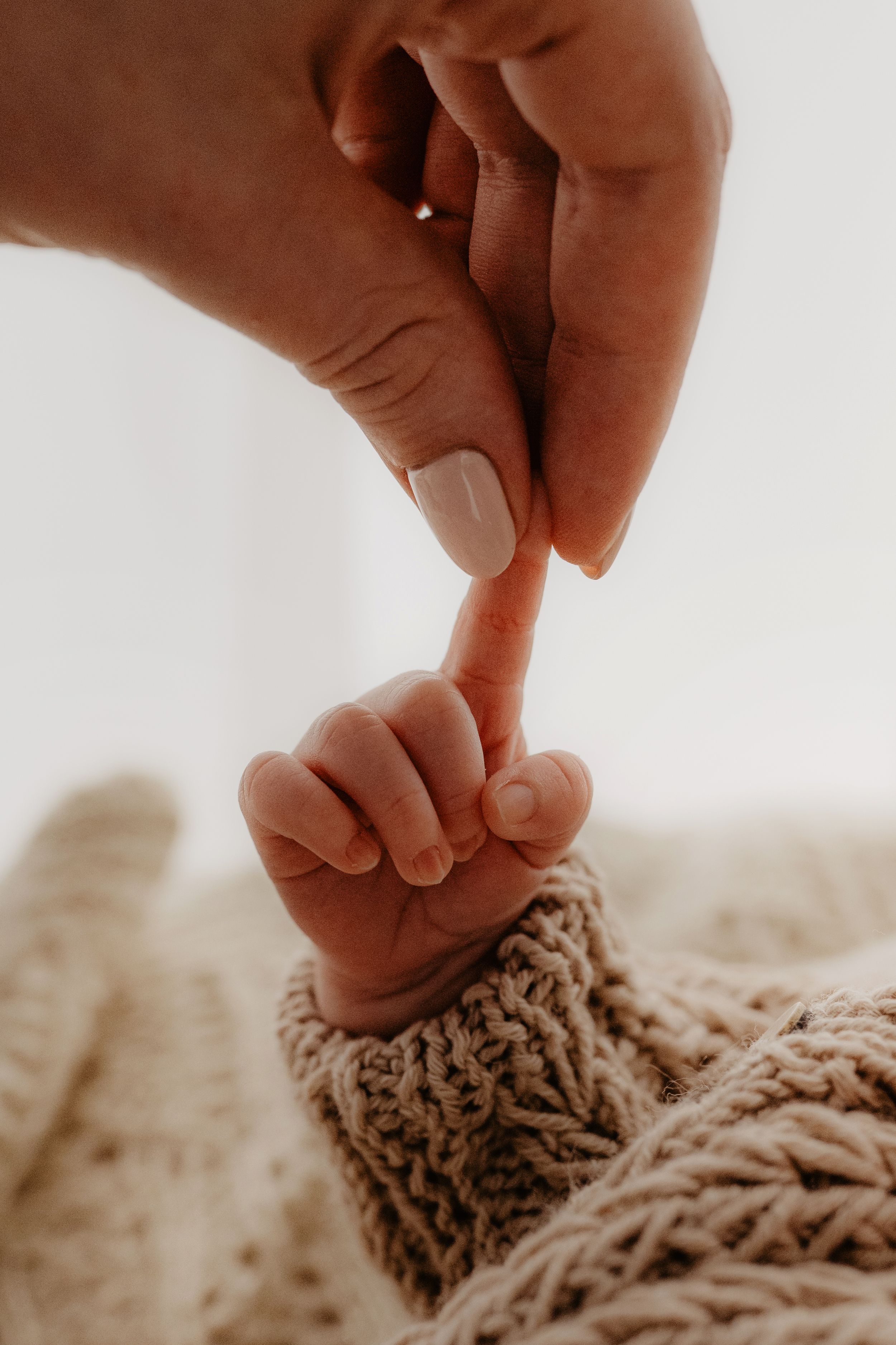 A tiny baby foot in a knit blanket touches an adult's finger in a tender moment.
