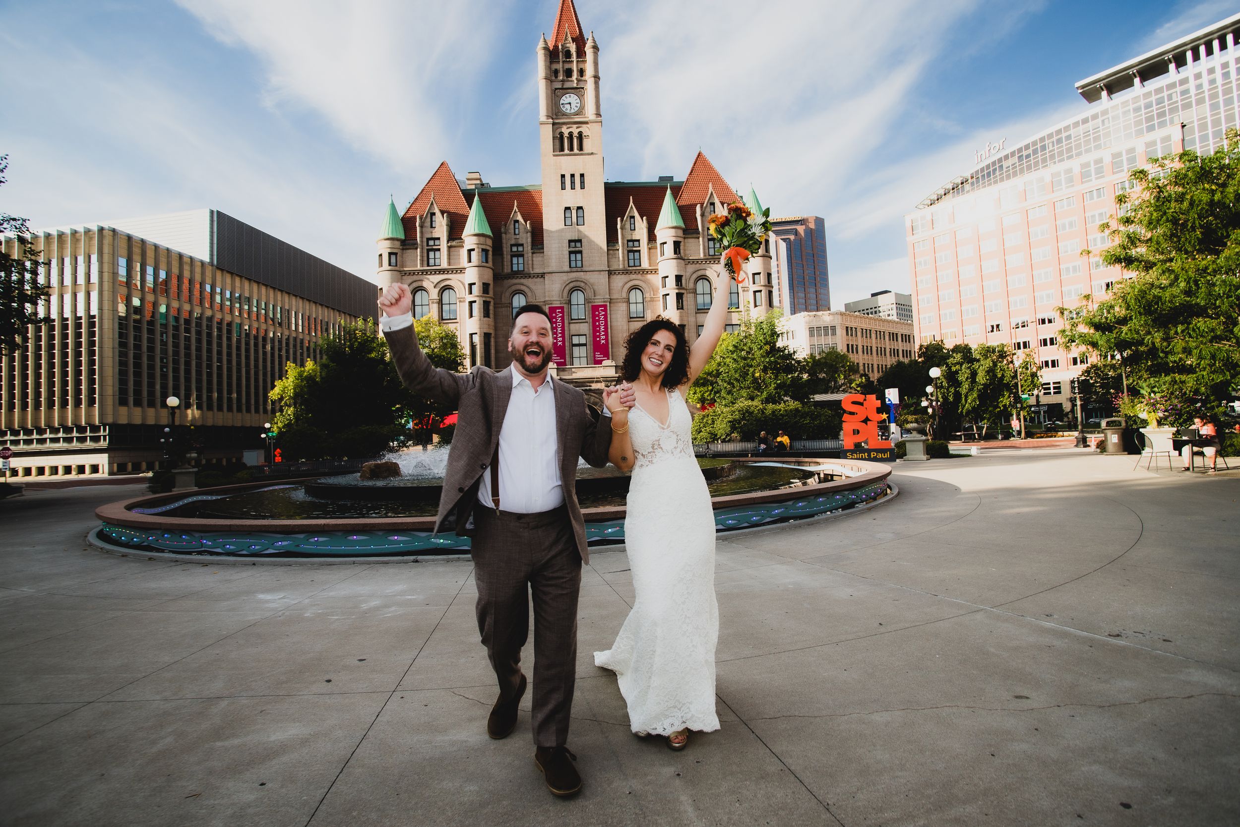 Wedding couple celebrating in front of historic landmark building with fountain.