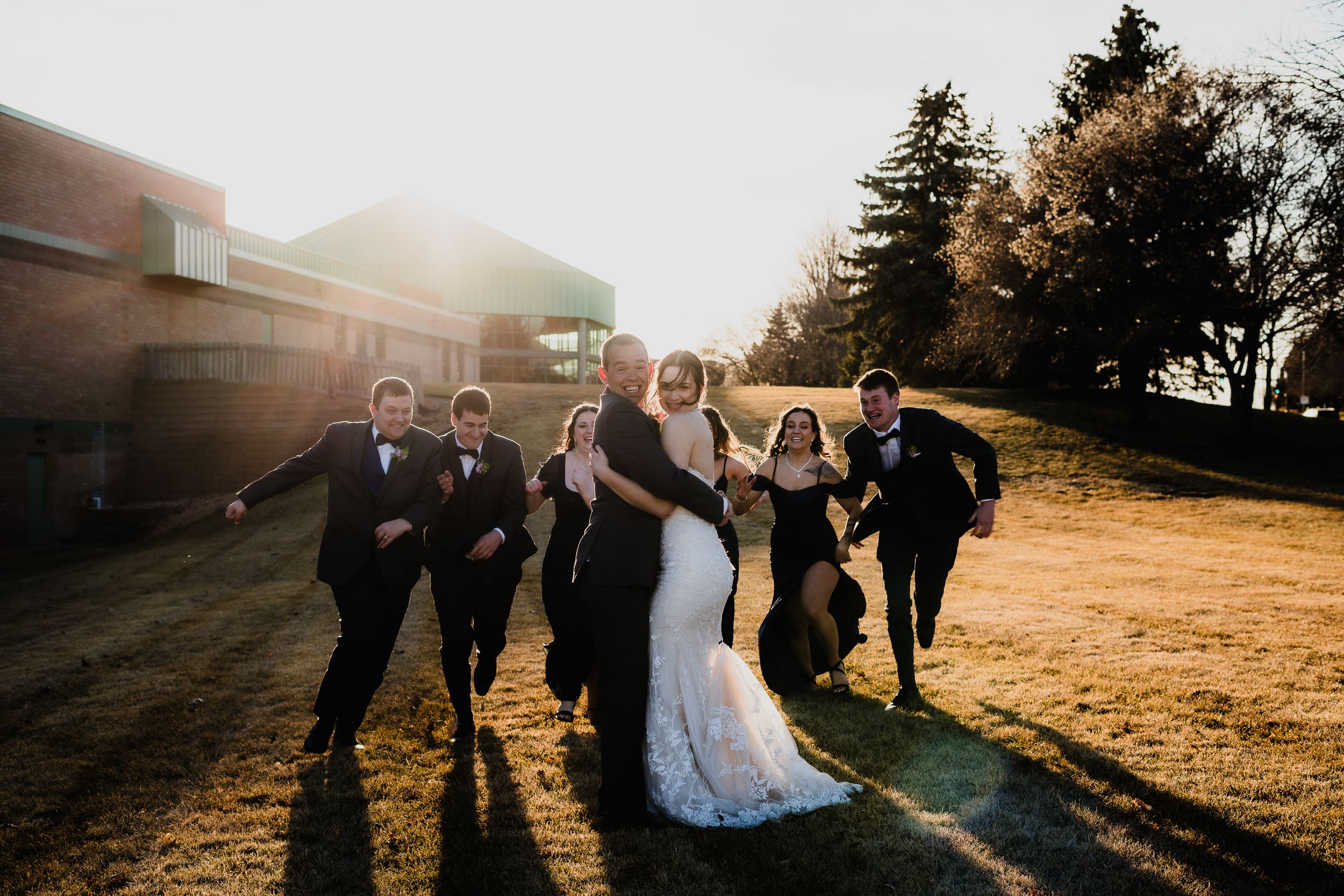 A wedding party poses together in golden sunlight on a hilltop.