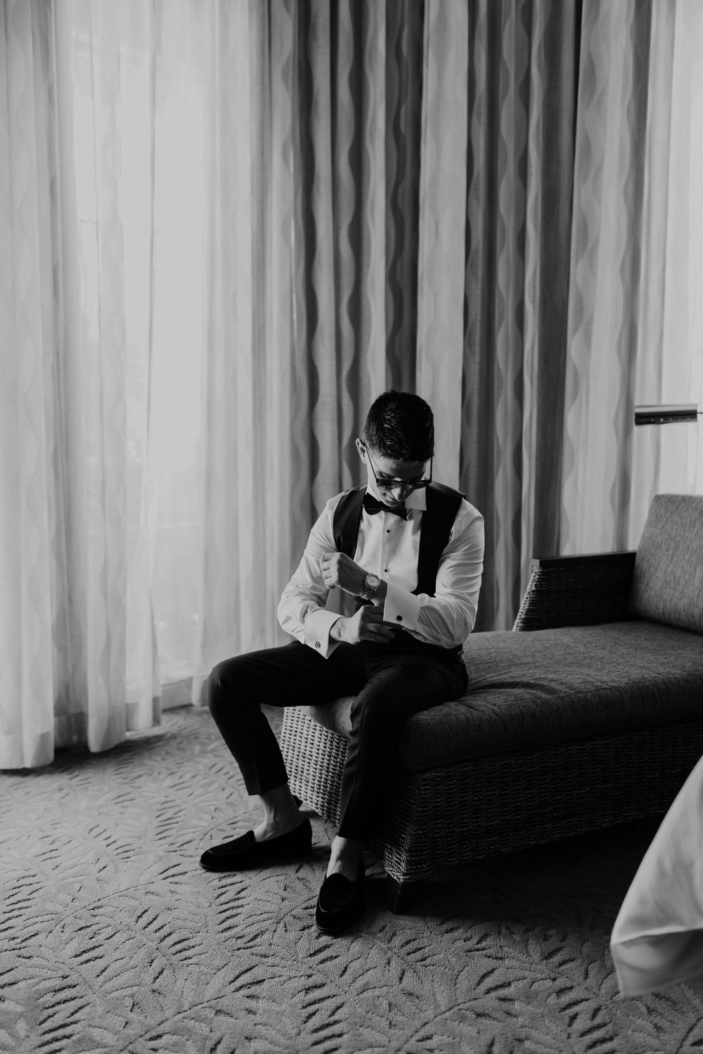 Wedding preparations scene with someone adjusting their bowtie on a couch.