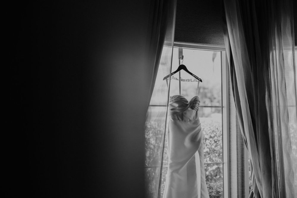 Wedding dress hanging in window silhouetted against natural light.