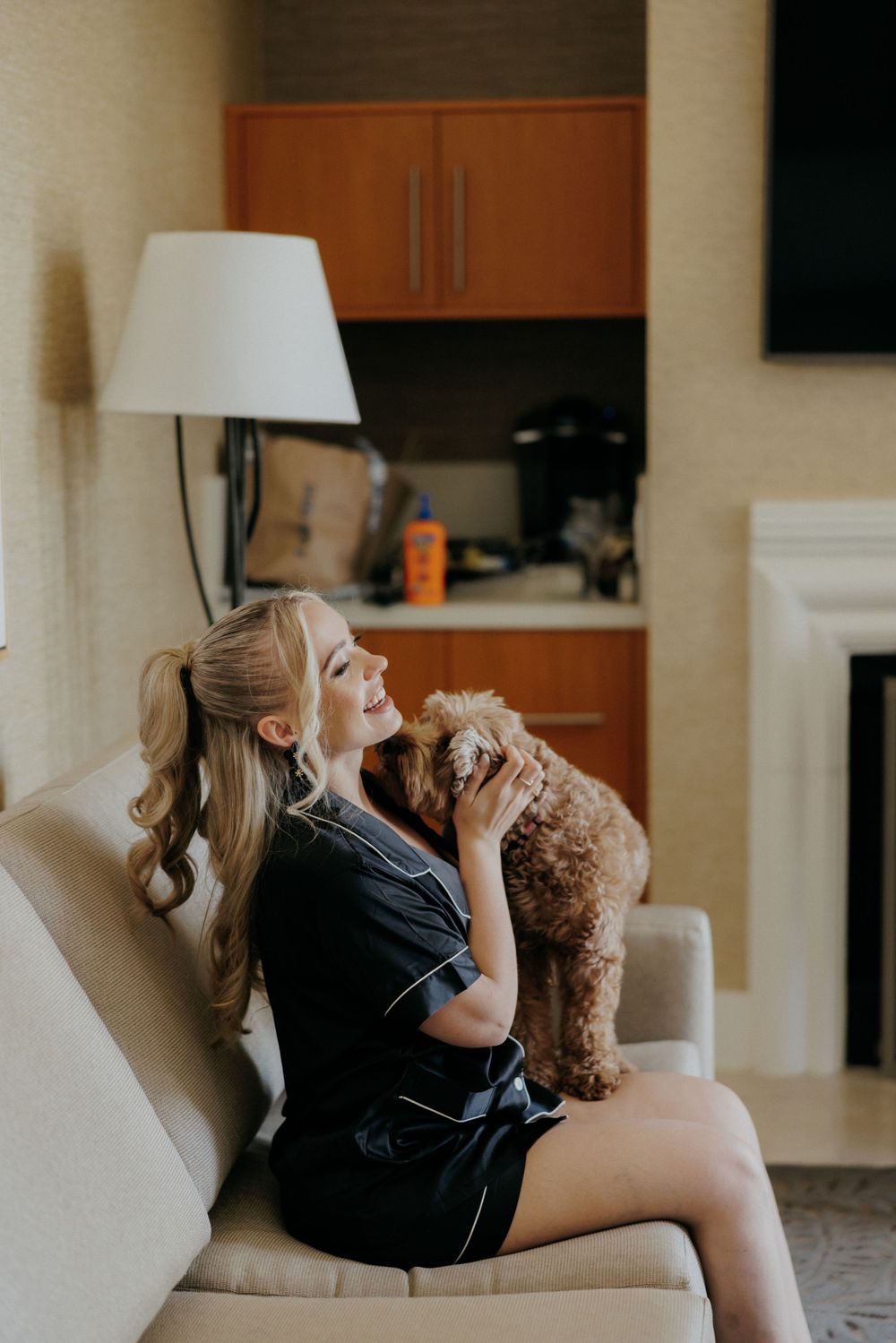 Person in black robe cuddling with goldendoodle dog on white couch.