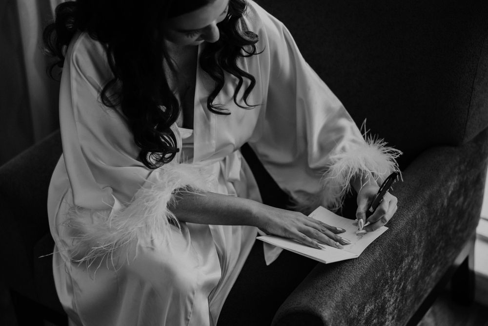 Person in white satin robe reading during wedding morning preparations in black and white photography.