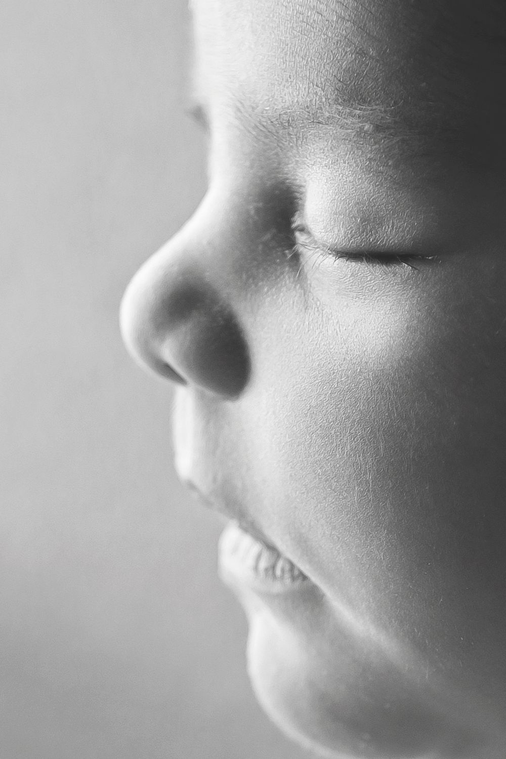 Close-up black and white profile portrait of a young child with closed eyes and soft skin.