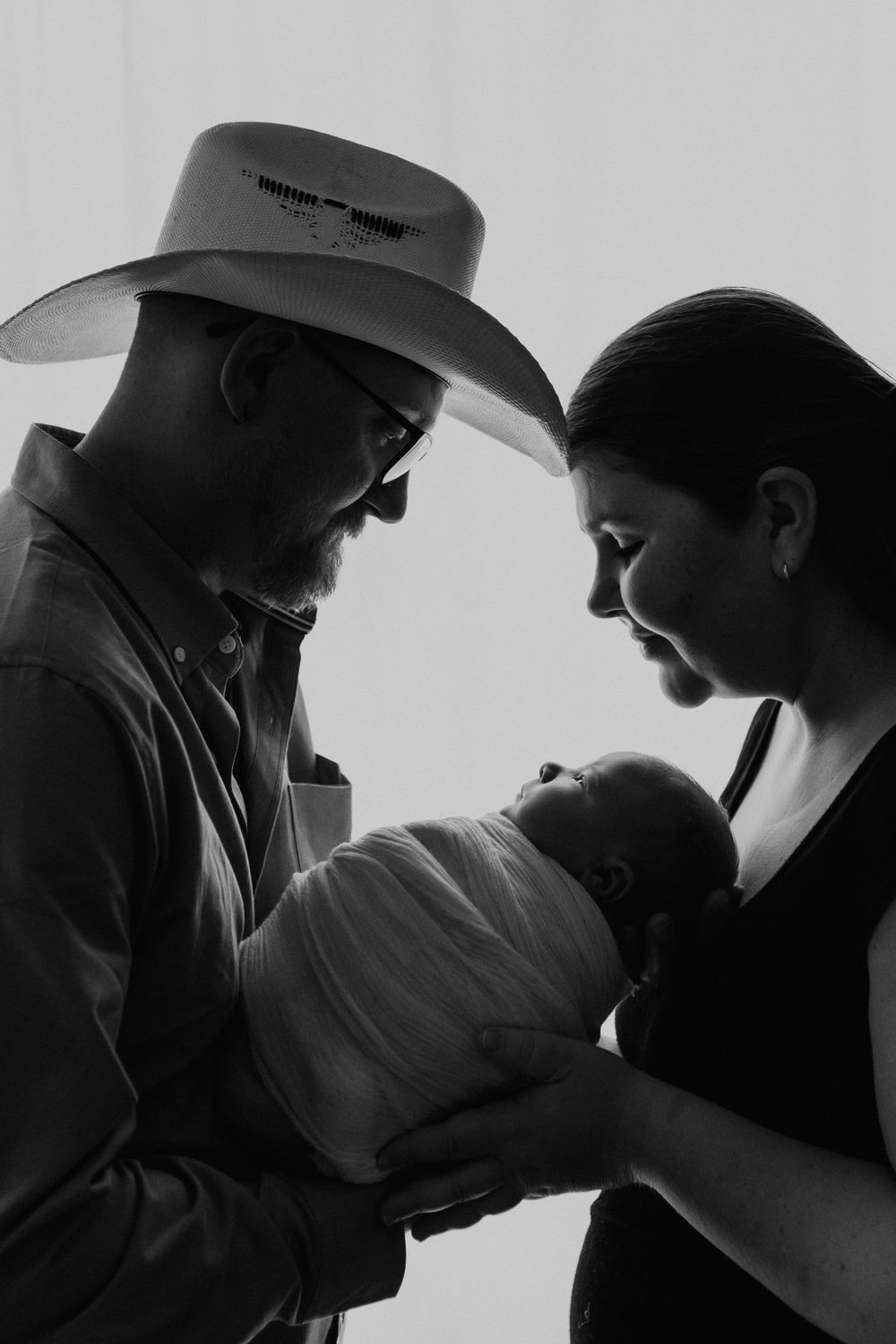 black and white image with mom and dad in cowboy hat holding newborn