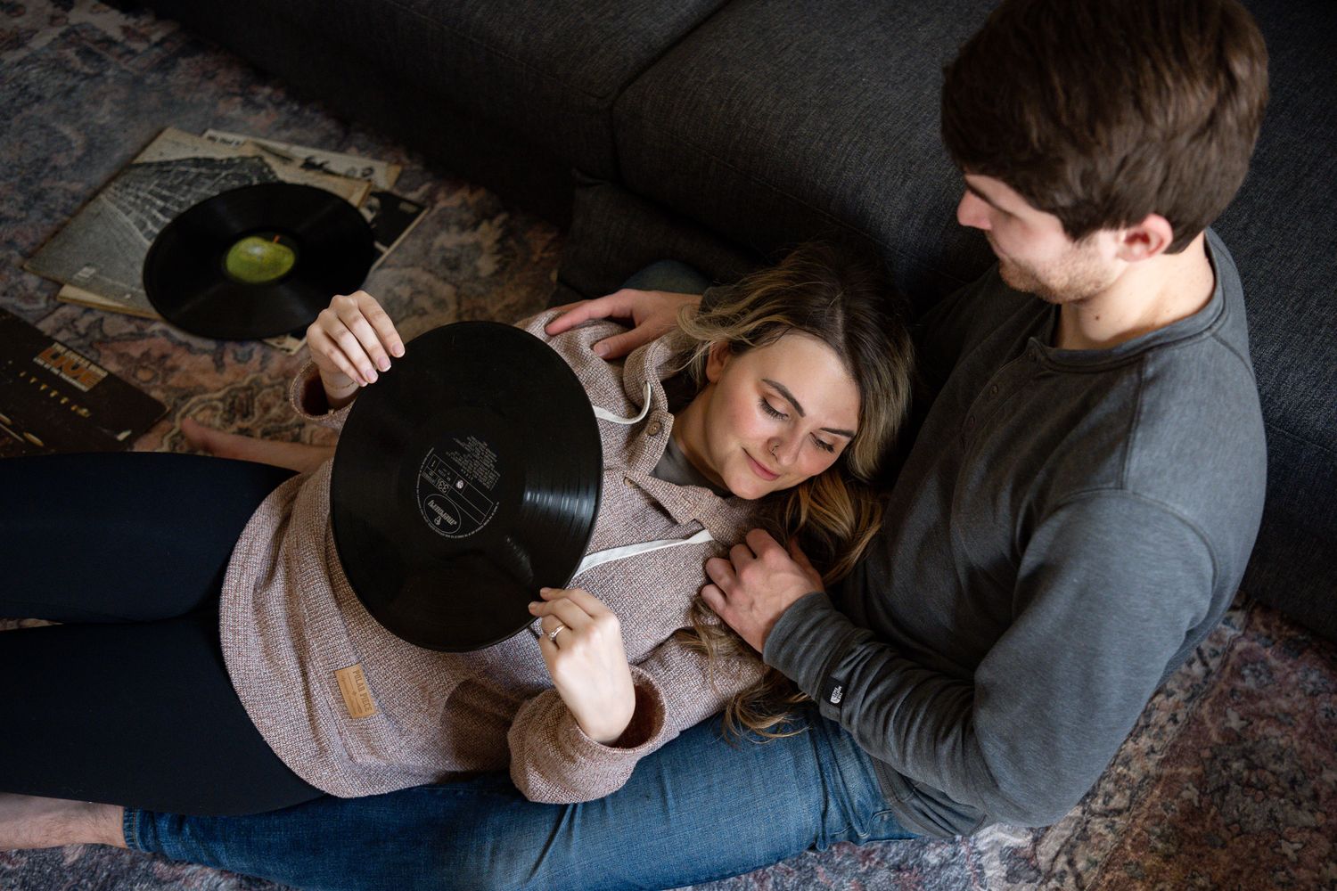 Two individuals listen to vintage vinyl records while relaxing on a patterned rug at home.