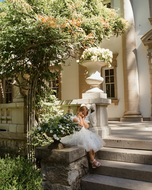 White tulle dress on architectural steps surrounded by blooming garden and climbing vines.