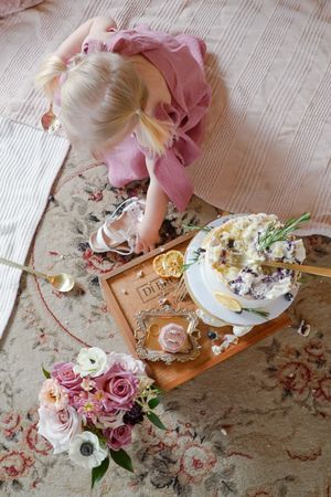 Overhead view of a person in pink dress looking down at floral table setting with roses and dessert on wooden board.