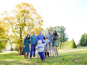 A group of people stand together on a grassy hill during a golden sunset photo session.