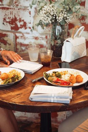 Several plates of food arranged on a rustic wooden round table with white napkins and drinks.