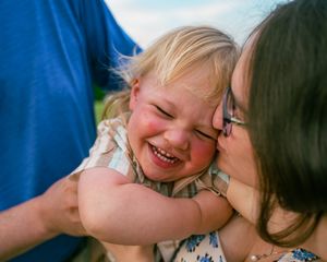 A laughing young child with blonde hair embraces and shares a joyful moment with an adult in glasses.