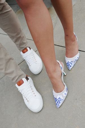 Row of feet wearing white sneakers mixed with blue and white floral print heels on concrete ground.