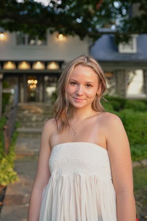 Evening portrait of someone in a white strapless dress with a house and garden in the background.