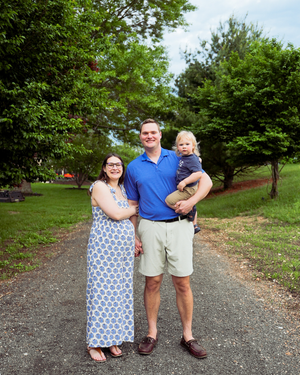 Family group walking together on a gravel path surrounded by lush green trees in a park setting.
