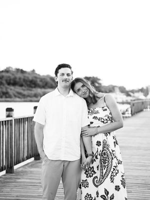 Five engagement photos on a beach boardwalk show a couple in casual white and floral attire at sunset.