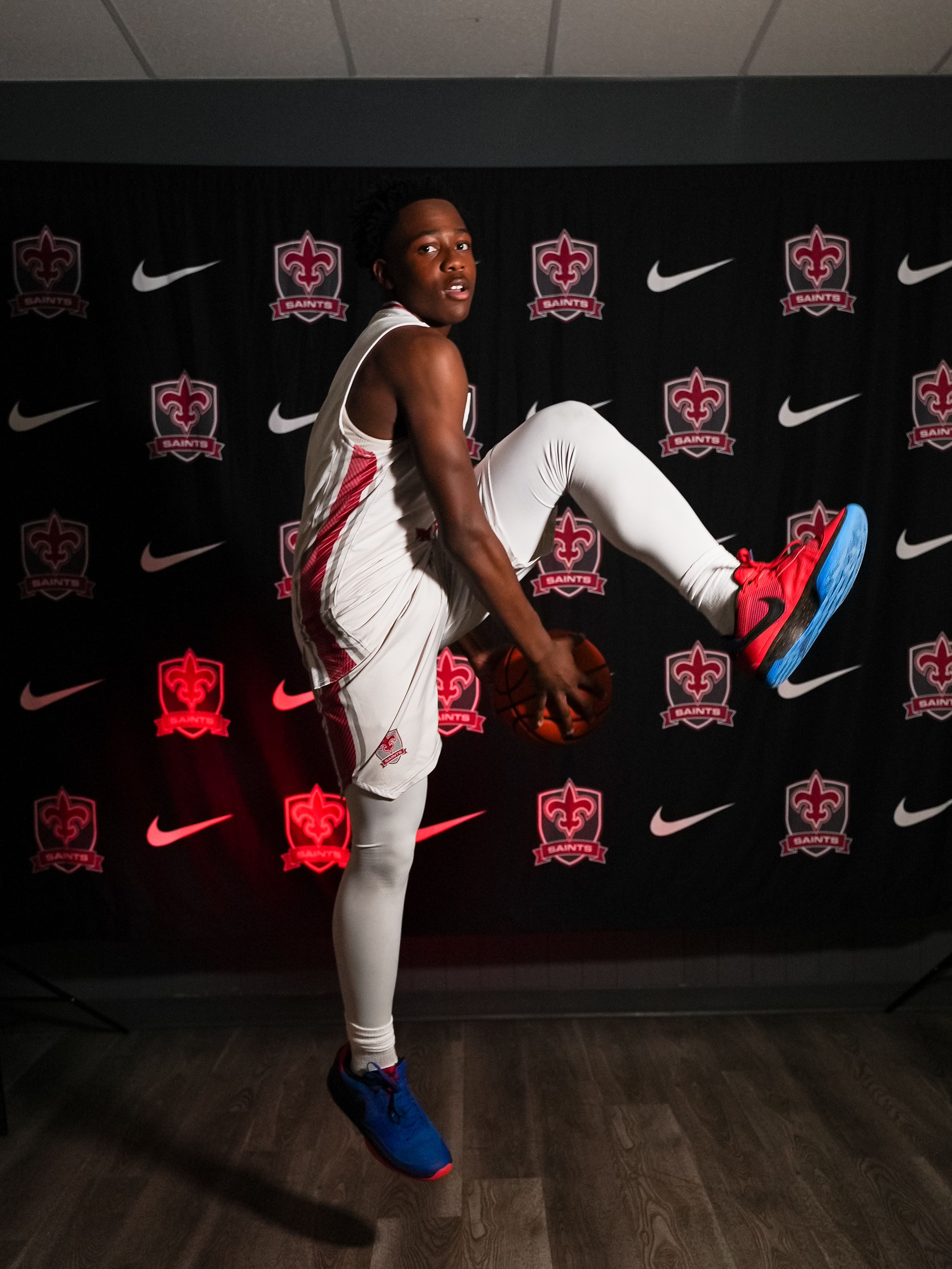 Athletic figure poses in white uniform against dark backdrop with red illuminated logos and Nike branding.