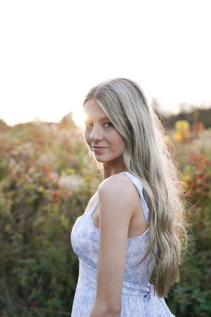 Backlit portrait in white dress with long hair against sunset garden backdrop.