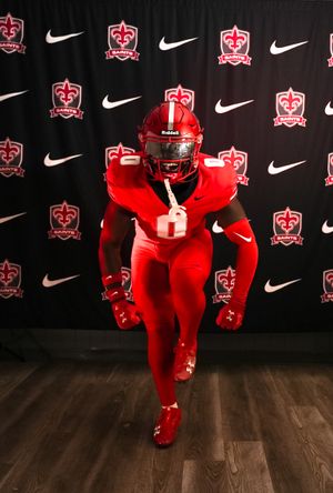 Football player in bright red uniform strikes dynamic pose against black backdrop with Nike logos.