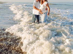 Couple standing in foamy ocean waves at the beach during sunset with water splashing around their feet.