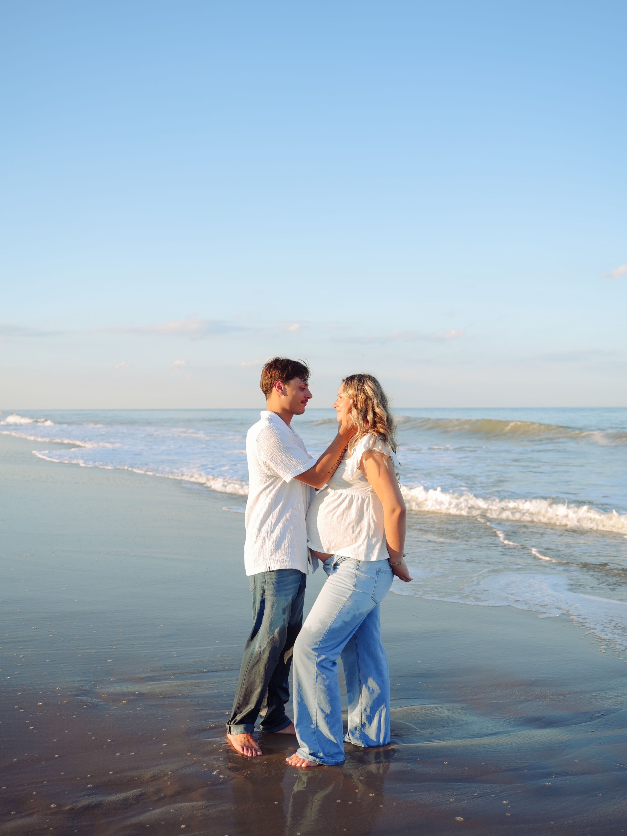 Couple dancing joyfully together on a scenic beach with waves and cloudy sky in the background.