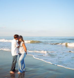 A couple walking hand in hand along a peaceful beach shoreline as waves gently roll in during golden hour.