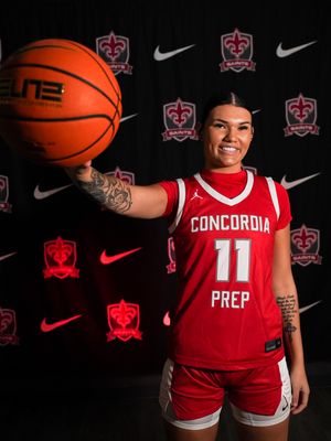 Basketball player in red Concordia Prep jersey poses with ball against dark background for sports photography session.