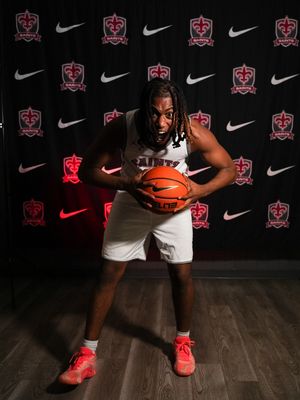 Basketball player poses in white uniform against backdrop of Nike and team logos during photo shoot.