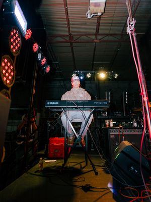 Musicians performing on a dimly lit stage with red LED lights and musical equipment visible in the background.
