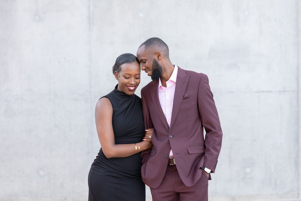 Elegantly dressed couple shares intimate moment against white wall background.