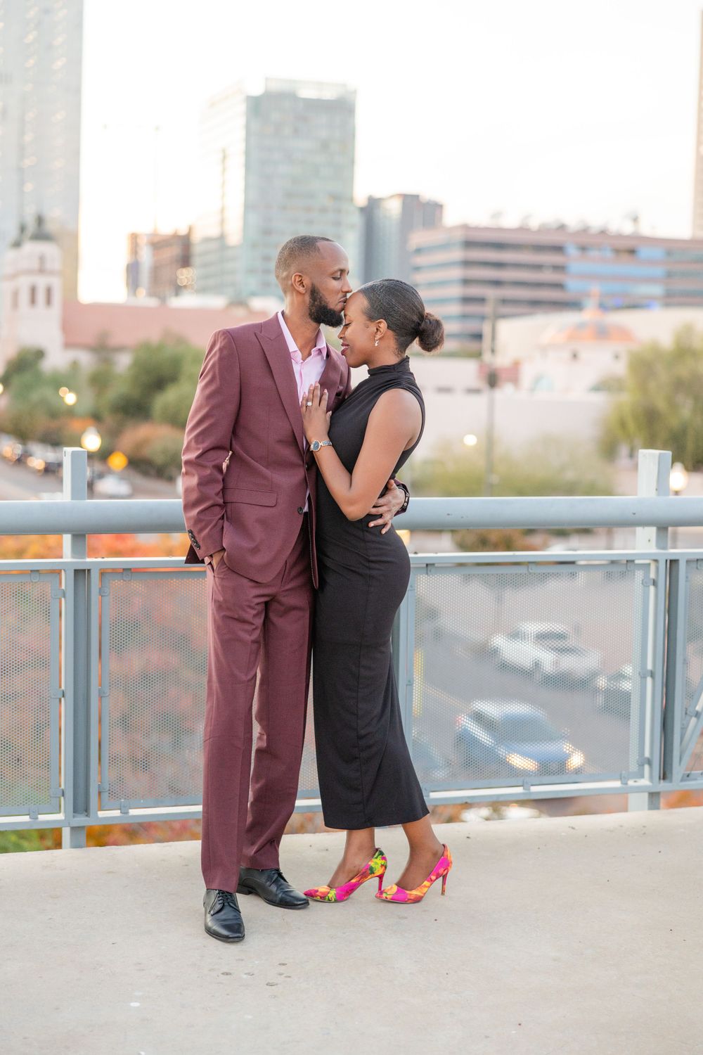 Romantic couple in formal wear embraces on urban rooftop during sunset.