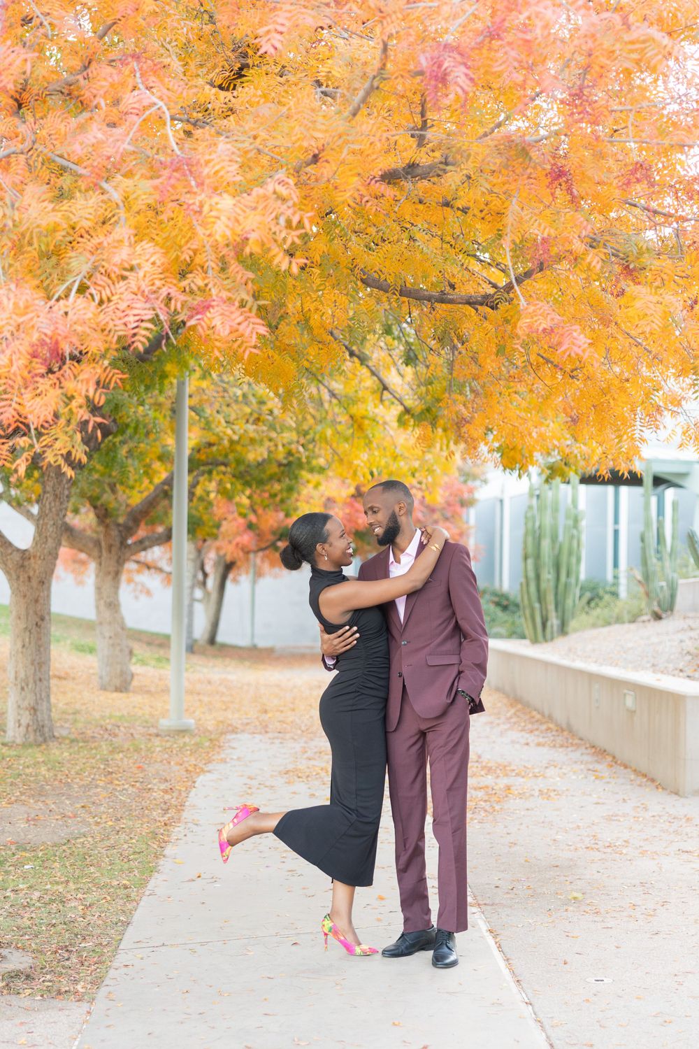 A couple embraces under vibrant autumn trees with orange foliage.