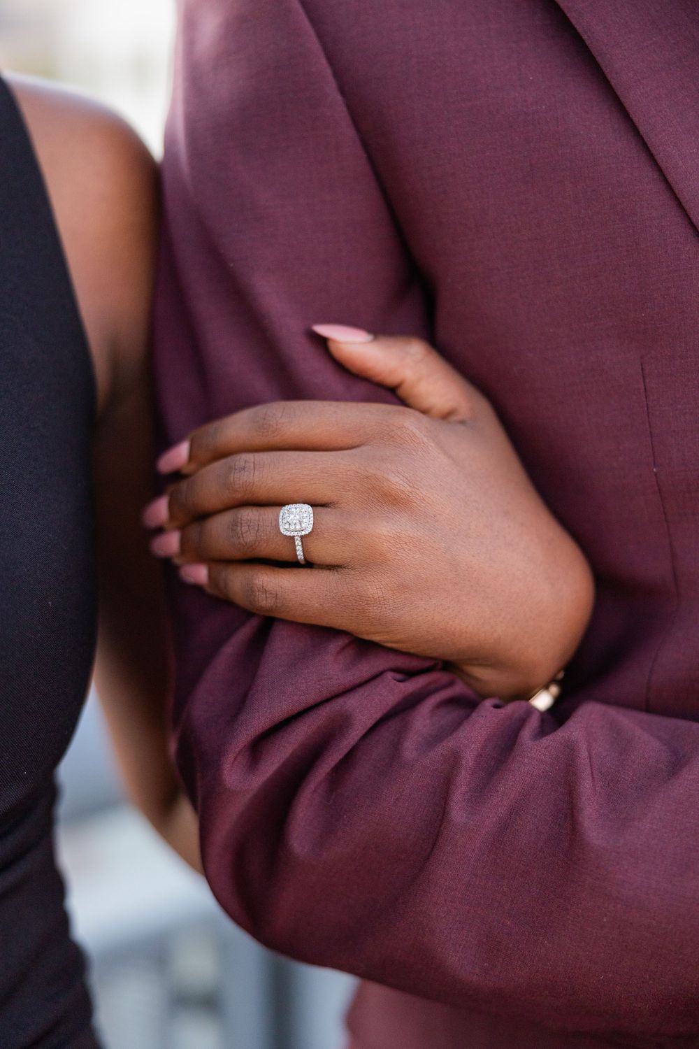 Close-up of an elegant diamond engagement ring on hand against burgundy suit fabric.