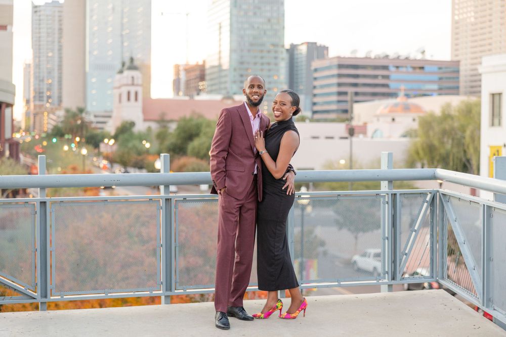 A couple poses romantically on a urban rooftop with city buildings in the background.