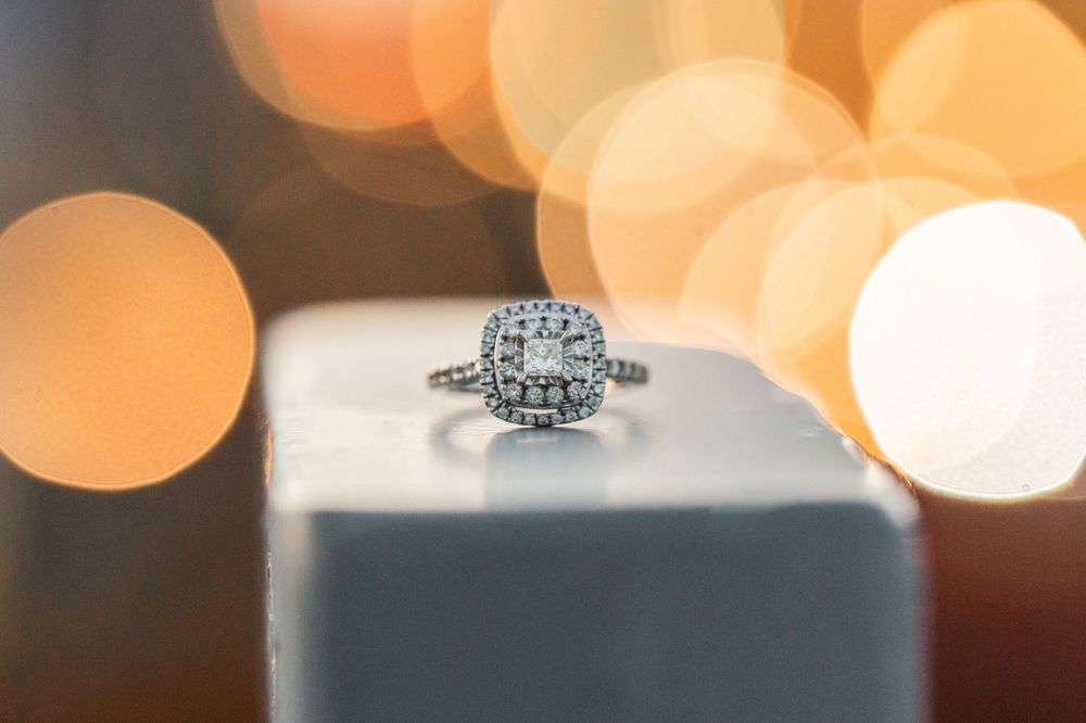 A diamond engagement ring photographed with soft bokeh lighting effects.