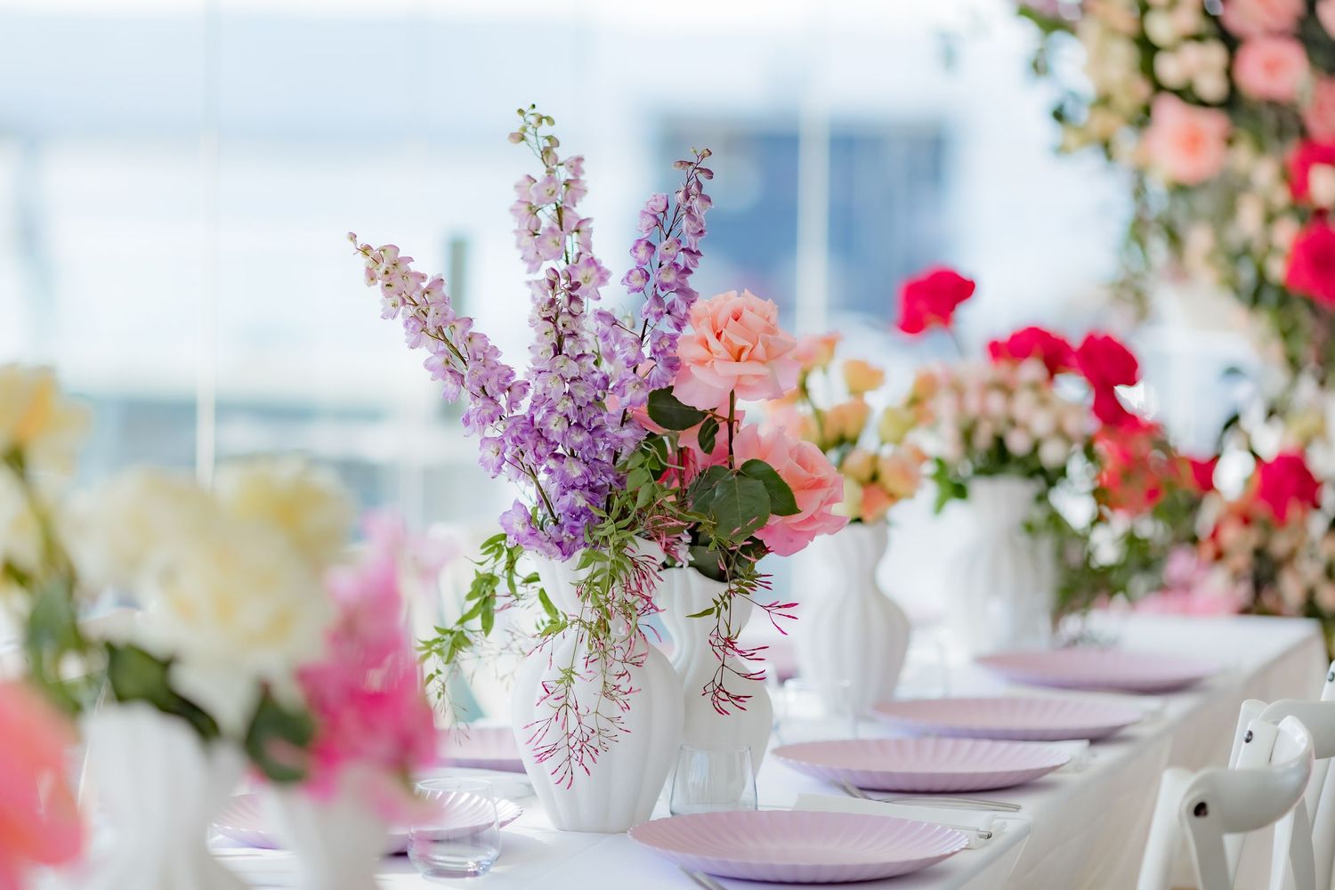 Table setting with purple and pink flowers in white vases and lilac place settings.