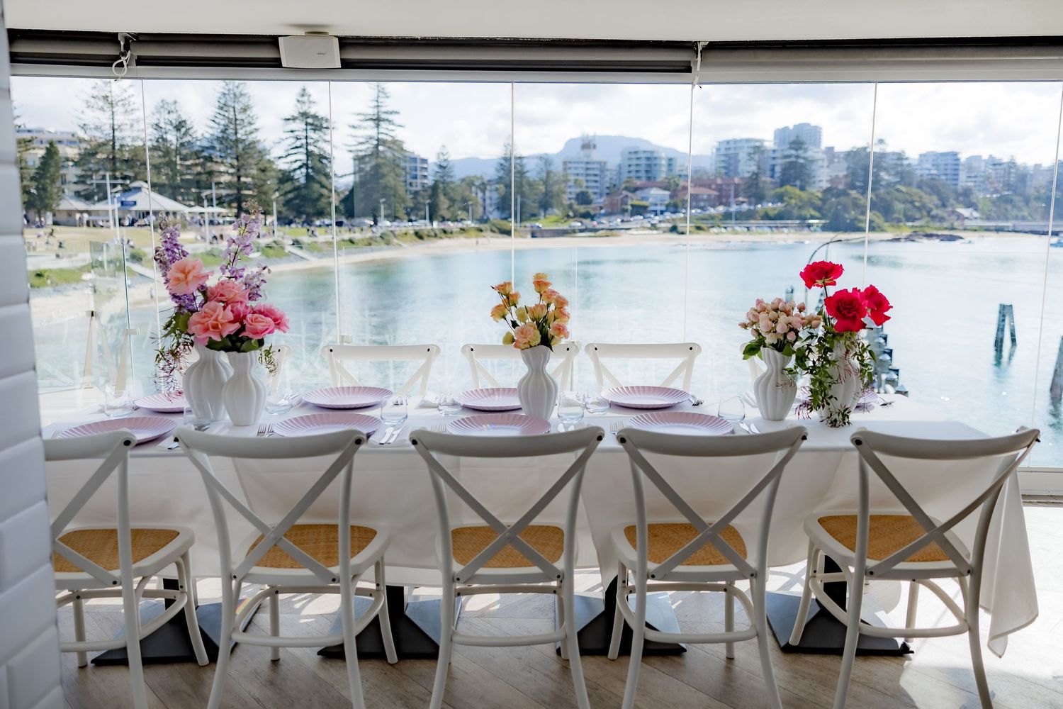 Waterfront dining setup with white chairs and floral centerpieces overlooking a scenic view.