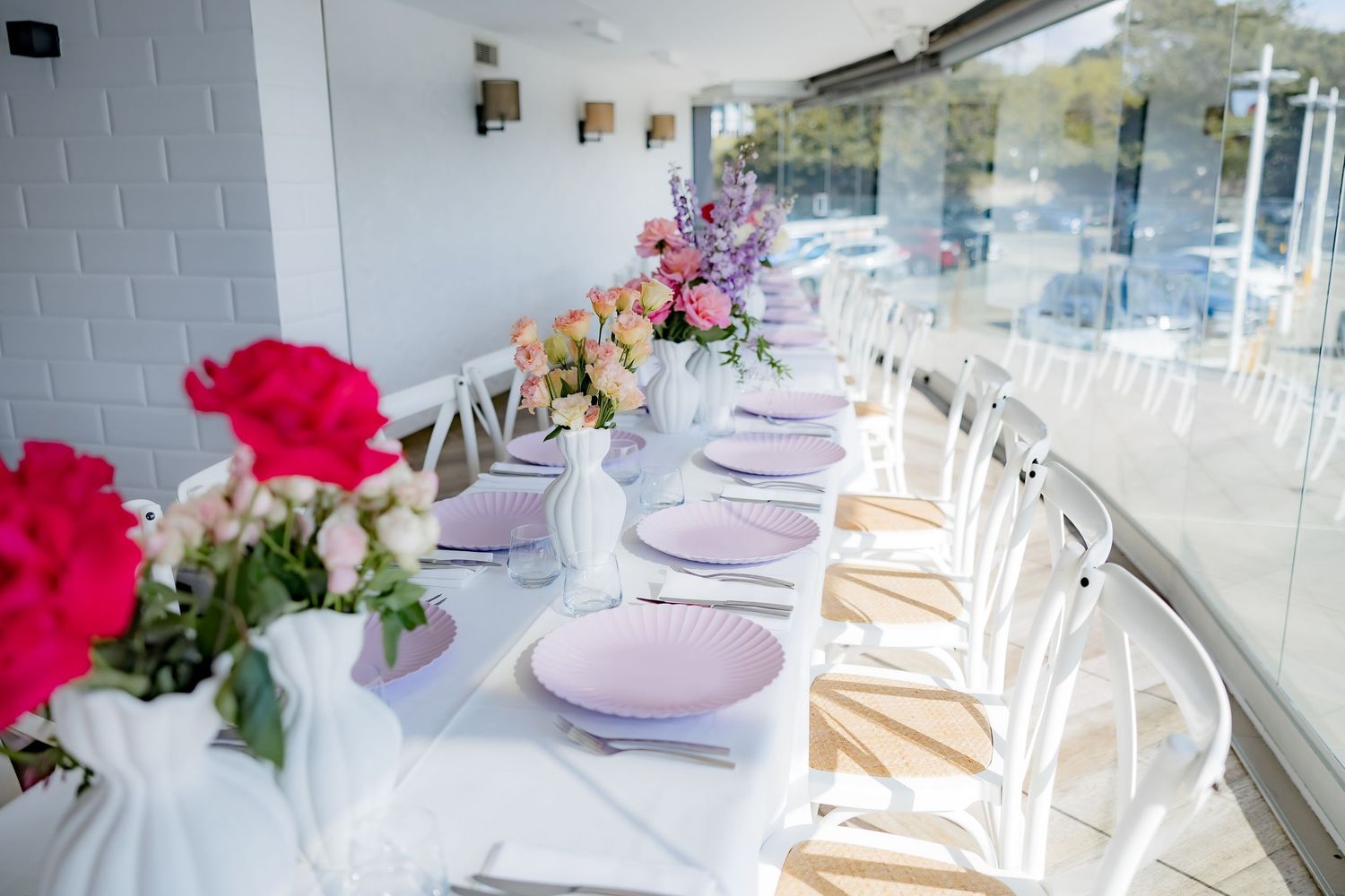 Elegant white dining table with pink place settings and bright floral arrangements.