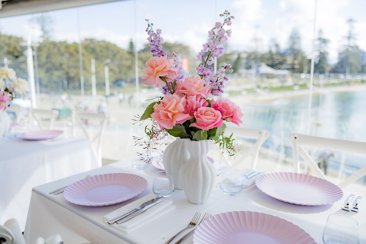 Table setting with pink plates and fresh floral centerpiece overlooking water view.