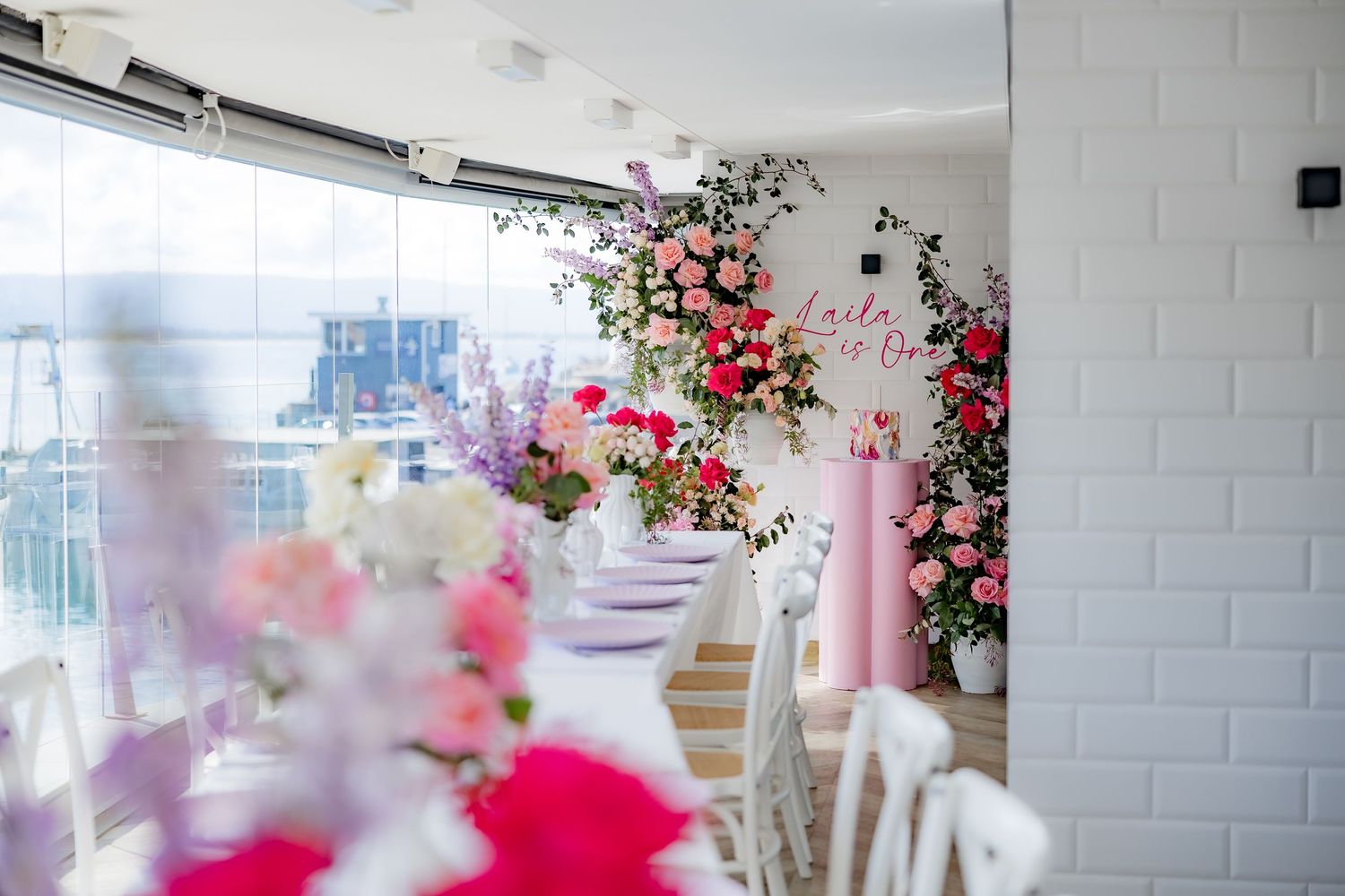 Pink and red floral arrangements adorning a white interior space with elegant table settings.