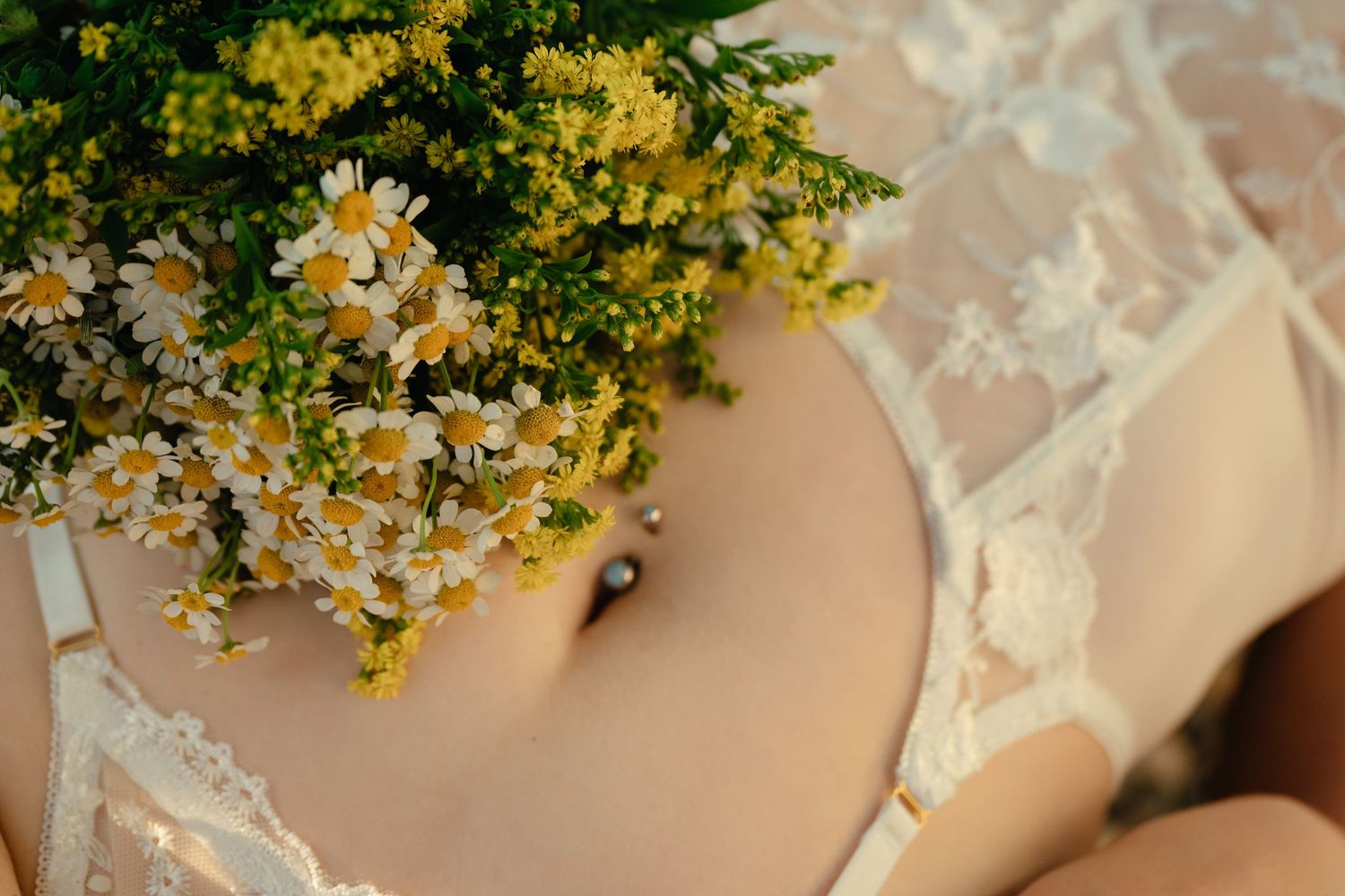 A delicate bouquet of white daisies and yellow flowers rests on a cream-colored lace dress.
