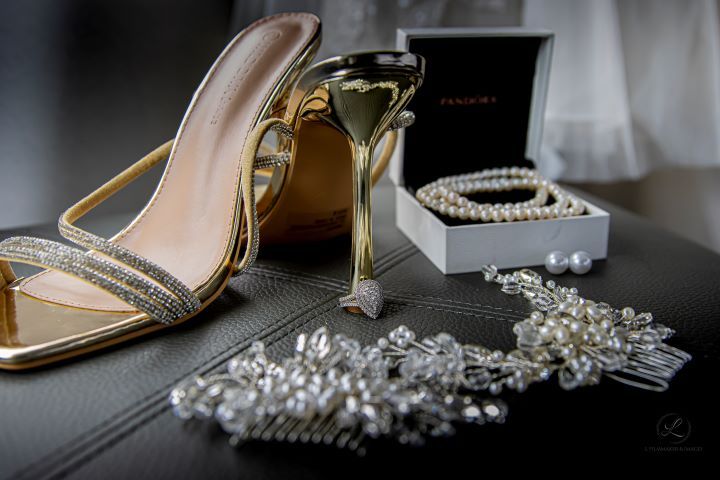 Close-up of sparkly bridal shoes and accessories on dark surface.