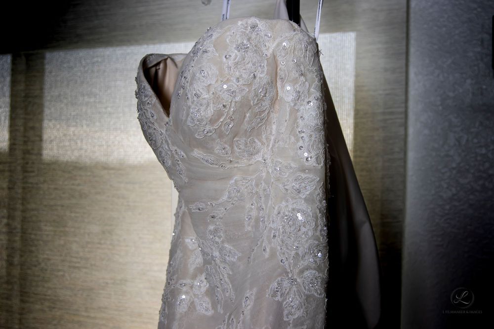 An elegant white lace wedding dress hangs against a light colored wall.