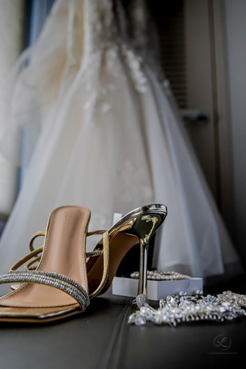 Wedding shoes and accessories arranged with white dress in background.