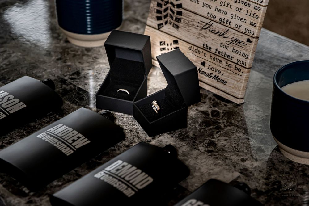 Wedding rings in black boxes alongside candles on marble surface.