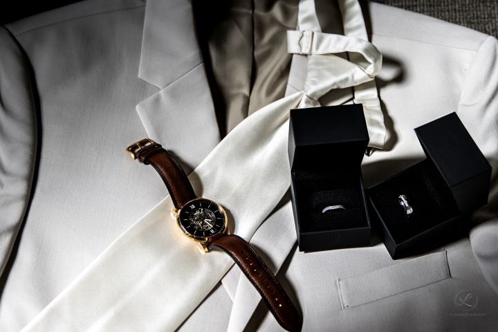 A white suit jacket with watch and ring boxes laid out.