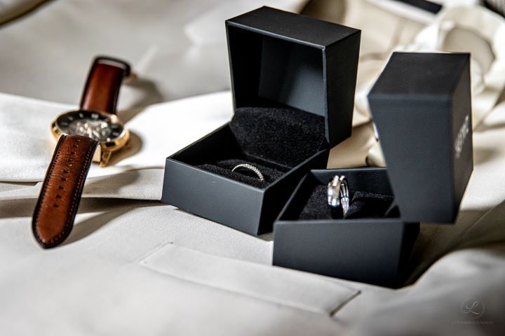 Wedding rings in black boxes with leather watch on white fabric.