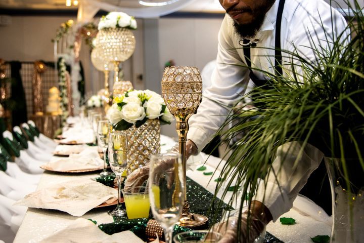 Wedding table setting featuring tall crystal centerpieces, white roses, and place settings with green accents.