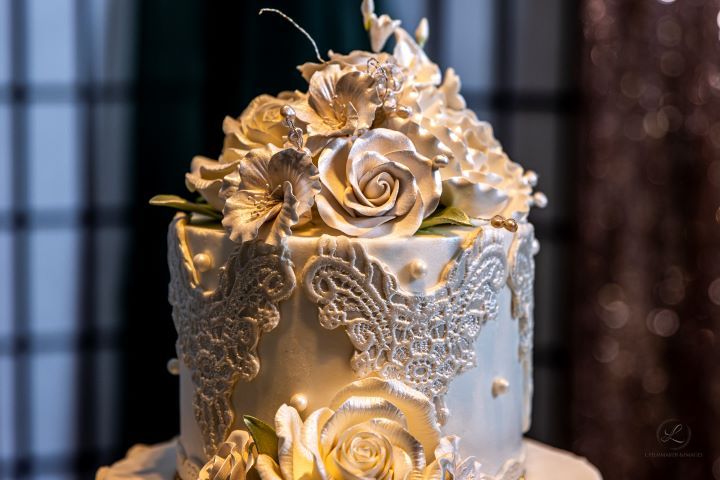 Elegant gold and white wedding cake decorated with metallic roses and intricate lace patterns.